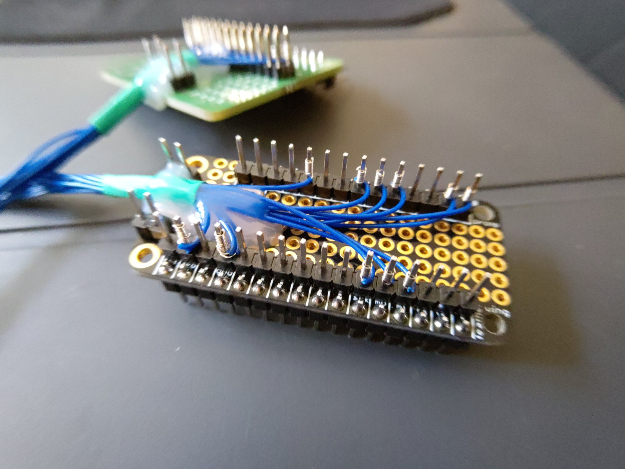A close-up of a FeatherWing Proto card, with a wire wrapped connector, and hot glue strain relief
